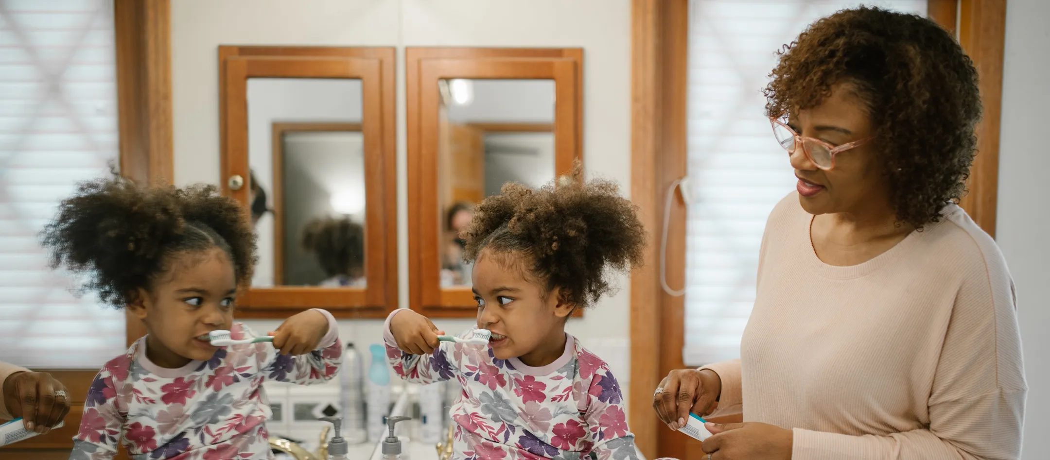 child brushes teeth in the mirror while female relative looks on and smiles